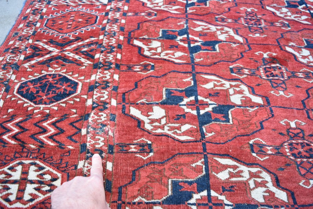 An antique hand-knotted Tekke Turkmen wool carpet featuring a repeating pattern of geometric octagonal guls on a deep red field with decorative geometric borders. View IX
