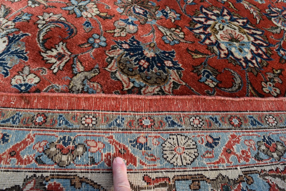 A large hand-knotted Persian Qum carpet featuring a detailed rust-red floral field framed by a wide light-blue decorative border. View VII