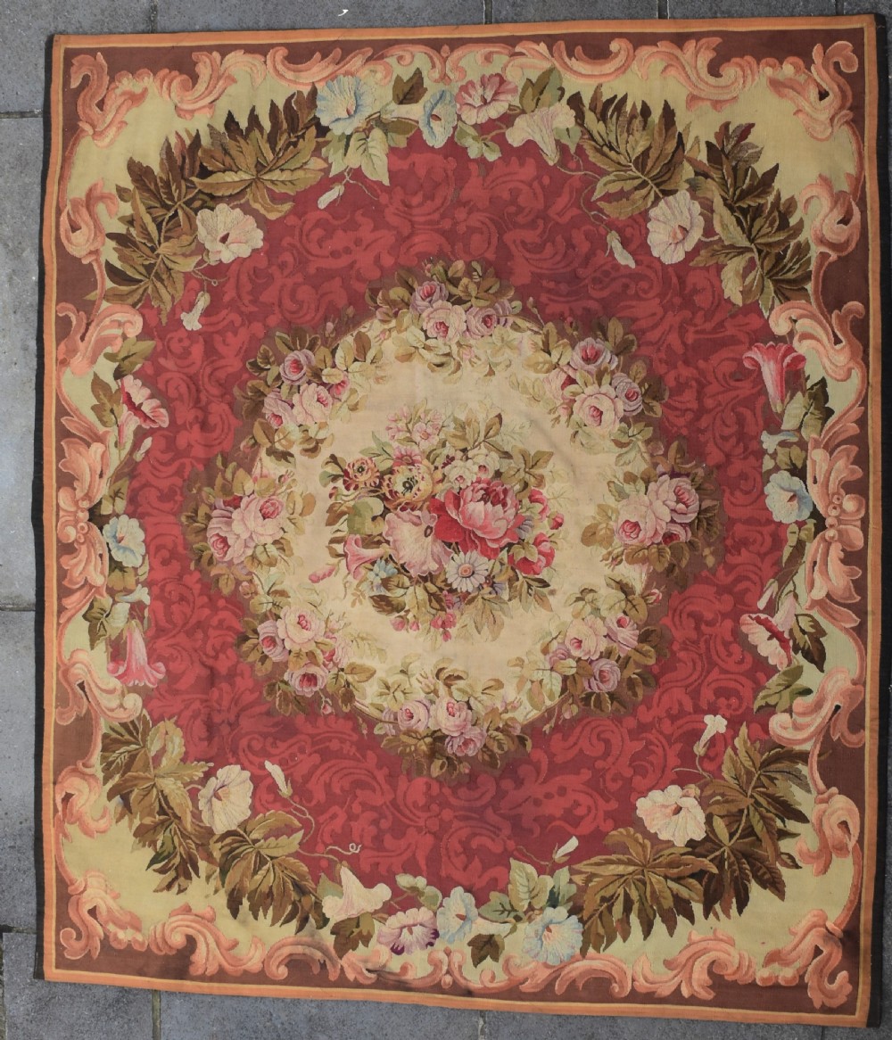 A square antique French Aubusson flatweave rug featuring a central pink floral medallion surrounded by a rose red field and ornate scroll borders.