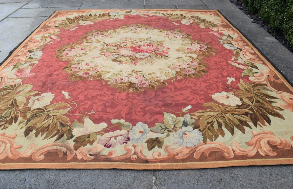 A square antique French Aubusson flatweave rug featuring a central pink floral medallion surrounded by a rose red field and ornate scroll borders. View III