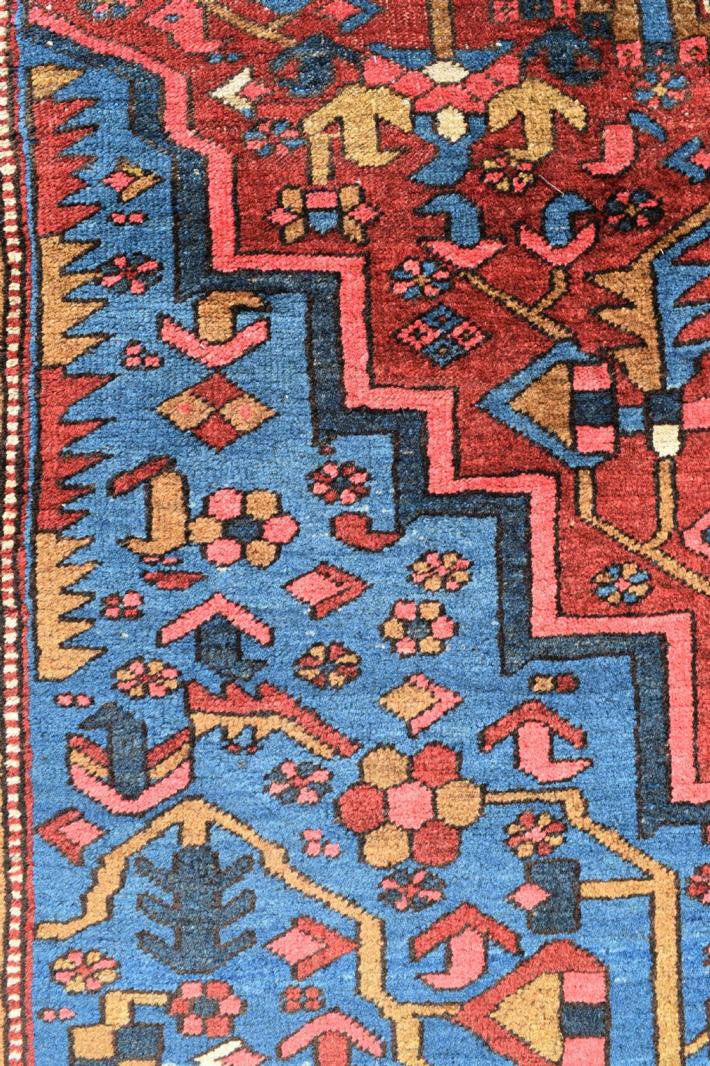 A large antique Persian Heriz wool carpet featuring a bold geometric central medallion, step-patterned spandrels in sky blue, and multi-layered decorative borders in terracotta, navy, and cream. View II