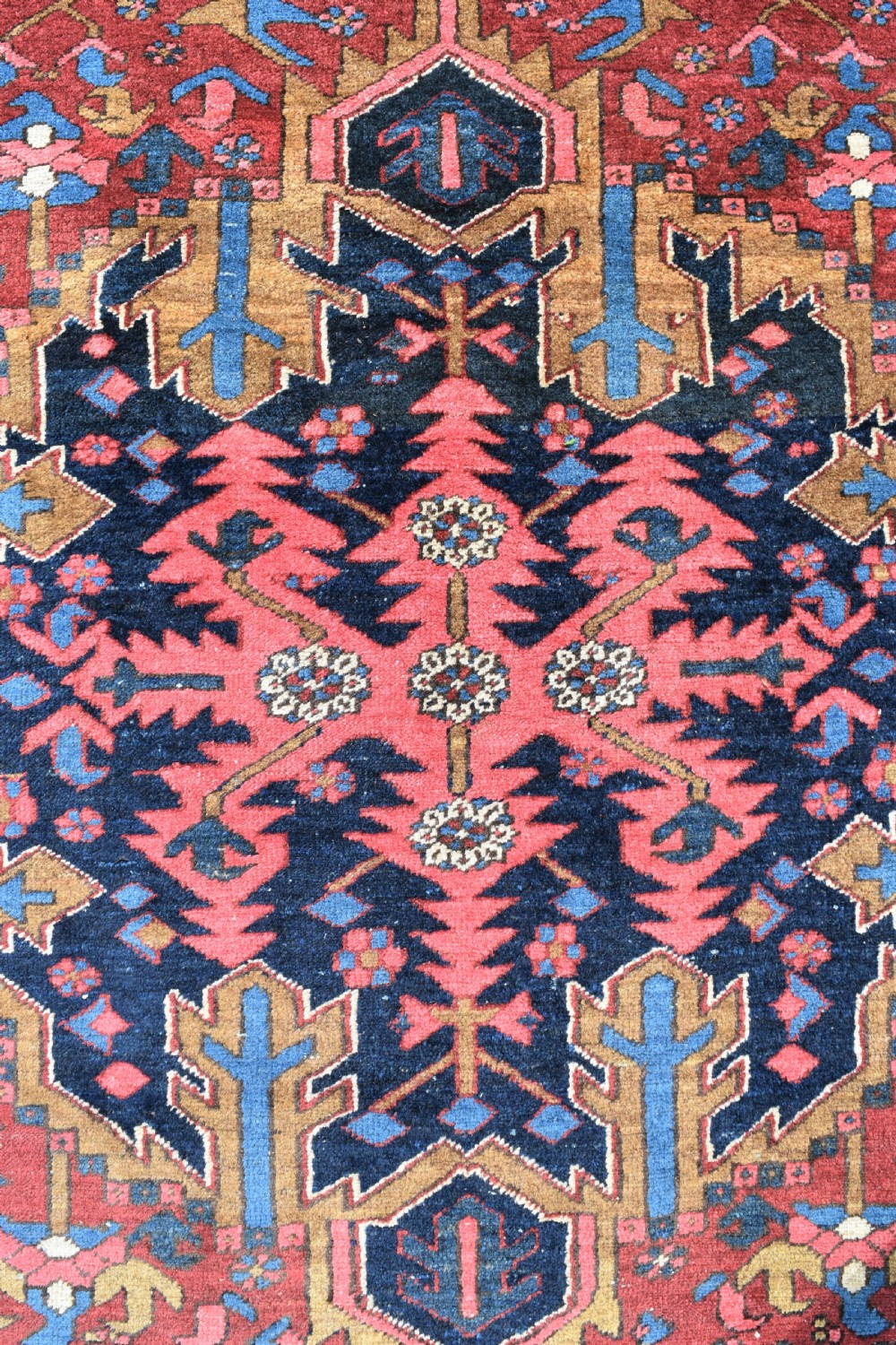 A large antique Persian Heriz wool carpet featuring a bold geometric central medallion, step-patterned spandrels in sky blue, and multi-layered decorative borders in terracotta, navy, and cream. View VIII