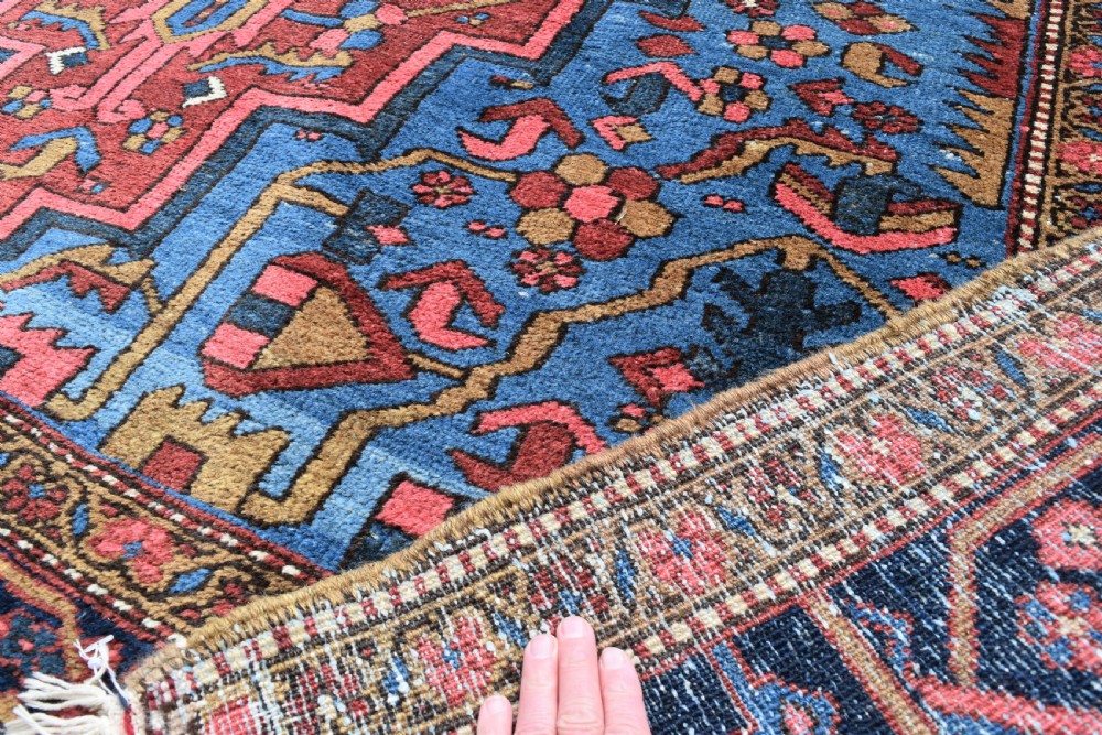 A large antique Persian Heriz wool carpet featuring a bold geometric central medallion, step-patterned spandrels in sky blue, and multi-layered decorative borders in terracotta, navy, and cream. View IX