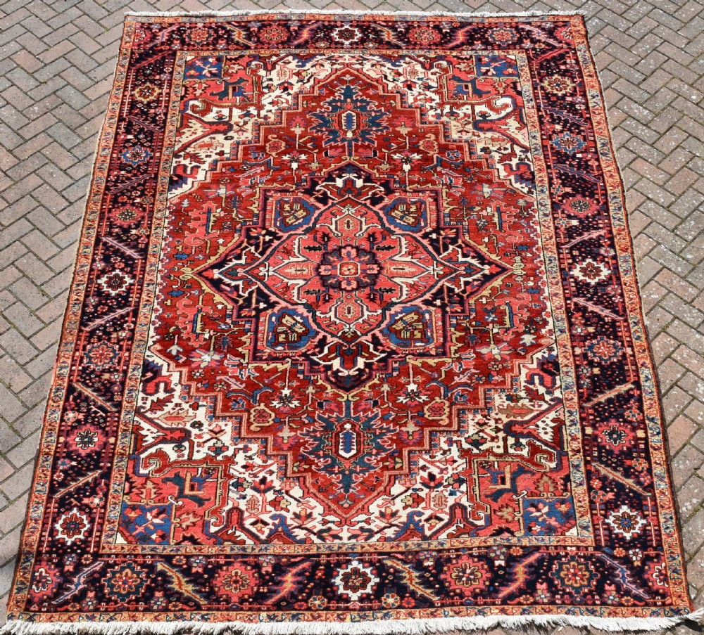 A room-sized hand-knotted Heriz carpet featuring a prominent geometric central medallion in terracotta red, navy blue, and ivory framed by a detailed border.