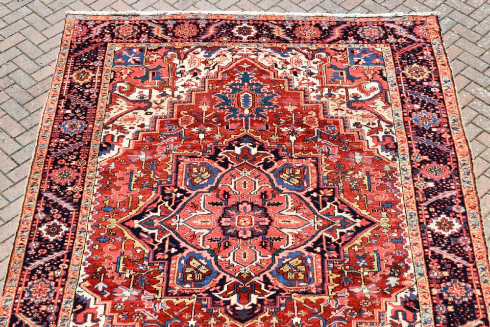 A room-sized hand-knotted Heriz carpet featuring a prominent geometric central medallion in terracotta red, navy blue, and ivory framed by a detailed border. View II