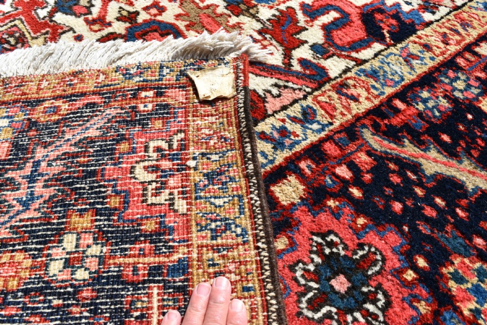 A room-sized hand-knotted Heriz carpet featuring a prominent geometric central medallion in terracotta red, navy blue, and ivory framed by a detailed border. View III