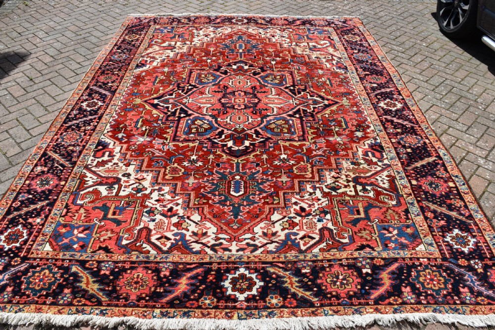 A room-sized hand-knotted Heriz carpet featuring a prominent geometric central medallion in terracotta red, navy blue, and ivory framed by a detailed border. View IV