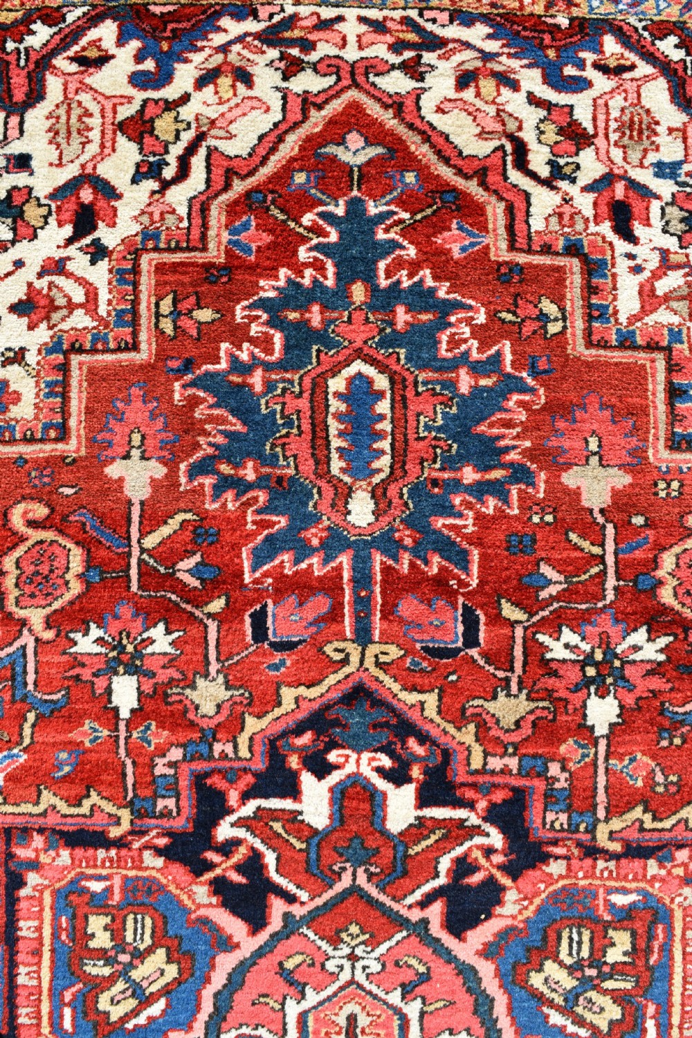 A room-sized hand-knotted Heriz carpet featuring a prominent geometric central medallion in terracotta red, navy blue, and ivory framed by a detailed border. View V