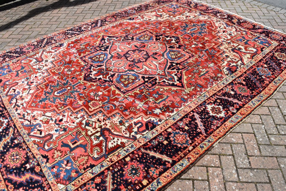 A room-sized hand-knotted Heriz carpet featuring a prominent geometric central medallion in terracotta red, navy blue, and ivory framed by a detailed border. View VI