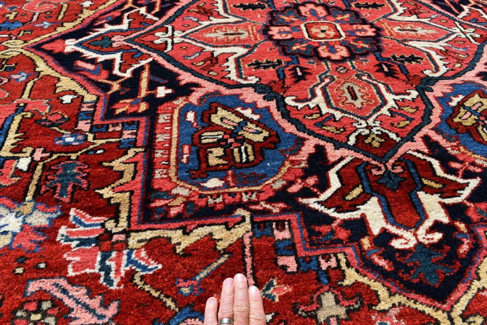 A room-sized hand-knotted Heriz carpet featuring a prominent geometric central medallion in terracotta red, navy blue, and ivory framed by a detailed border. View VII