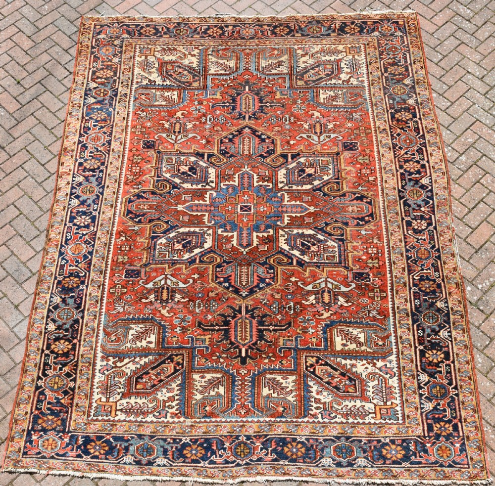 A large antique Heriz room-size carpet displaying a prominent geometric central medallion in navy blue, terracotta red, and cream tones.