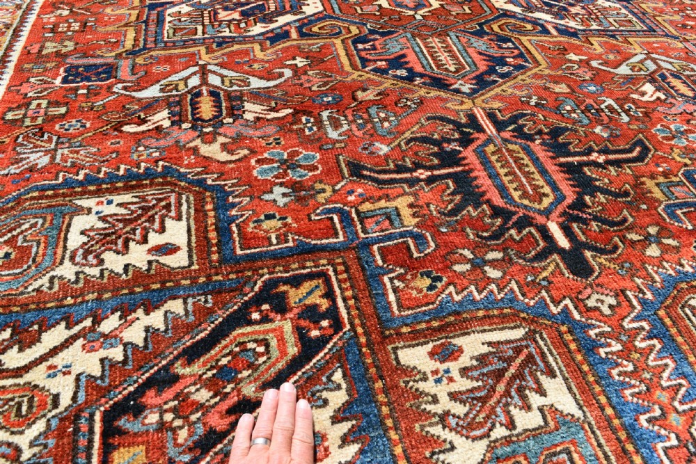 A large antique Heriz room-size carpet displaying a prominent geometric central medallion in navy blue, terracotta red, and cream tones. View VII