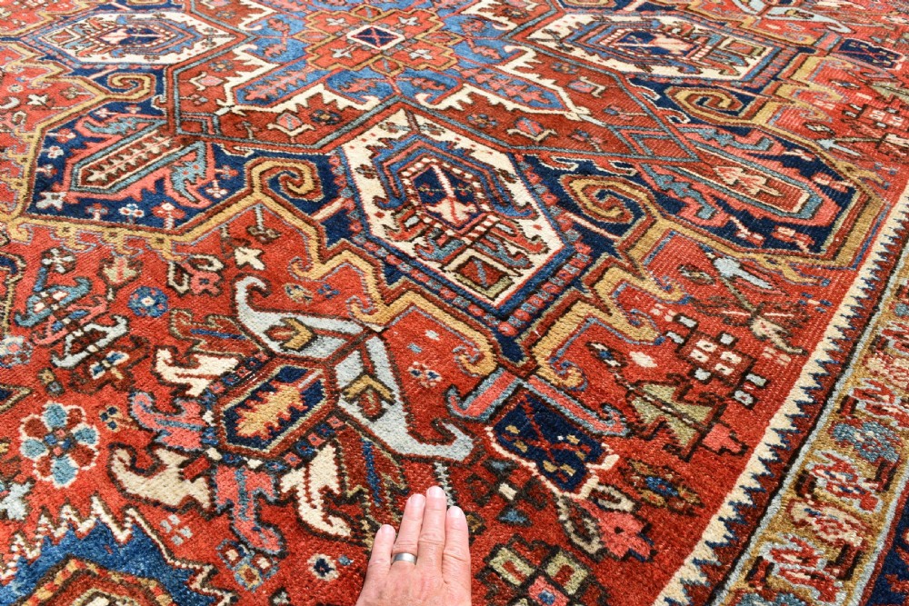 A large antique Heriz room-size carpet displaying a prominent geometric central medallion in navy blue, terracotta red, and cream tones. View VIII