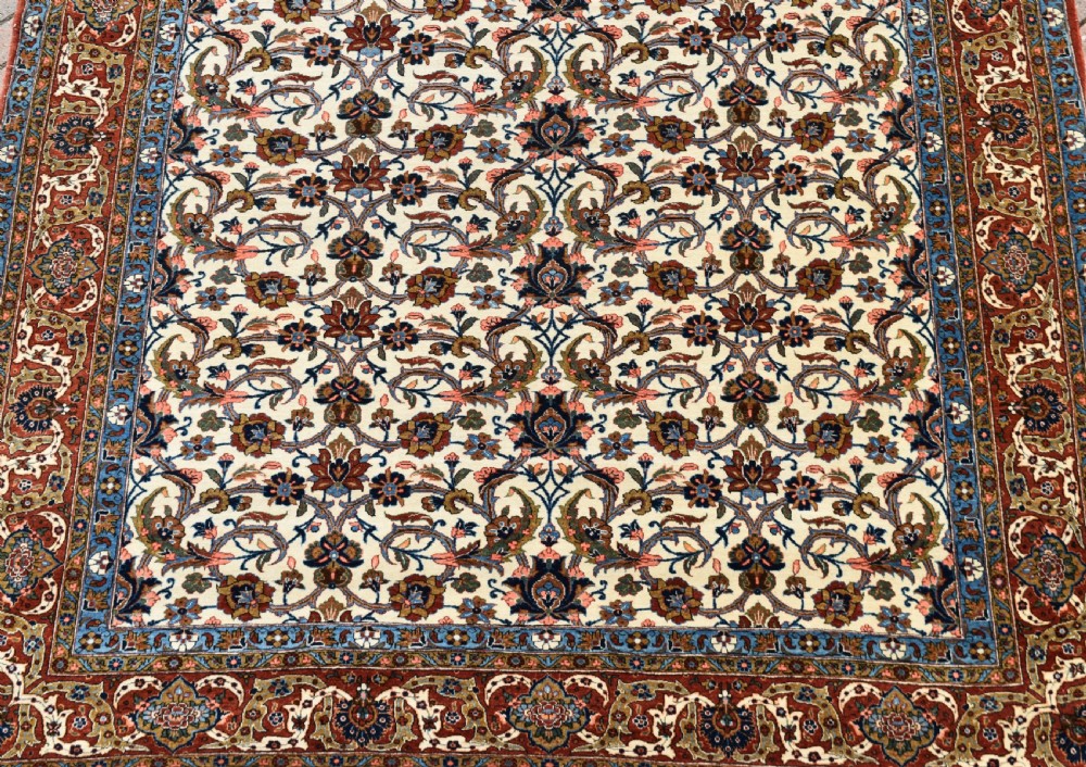 A large hand-knotted Persian Qum carpet featuring an all-over intricate floral vine motif on an ivory field, framed by multi-tiered red and blue decorative borders with fringe ends. View II