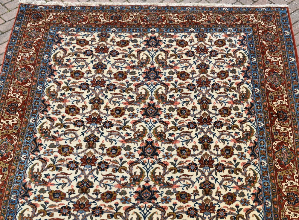 A large hand-knotted Persian Qum carpet featuring an all-over intricate floral vine motif on an ivory field, framed by multi-tiered red and blue decorative borders with fringe ends. View III