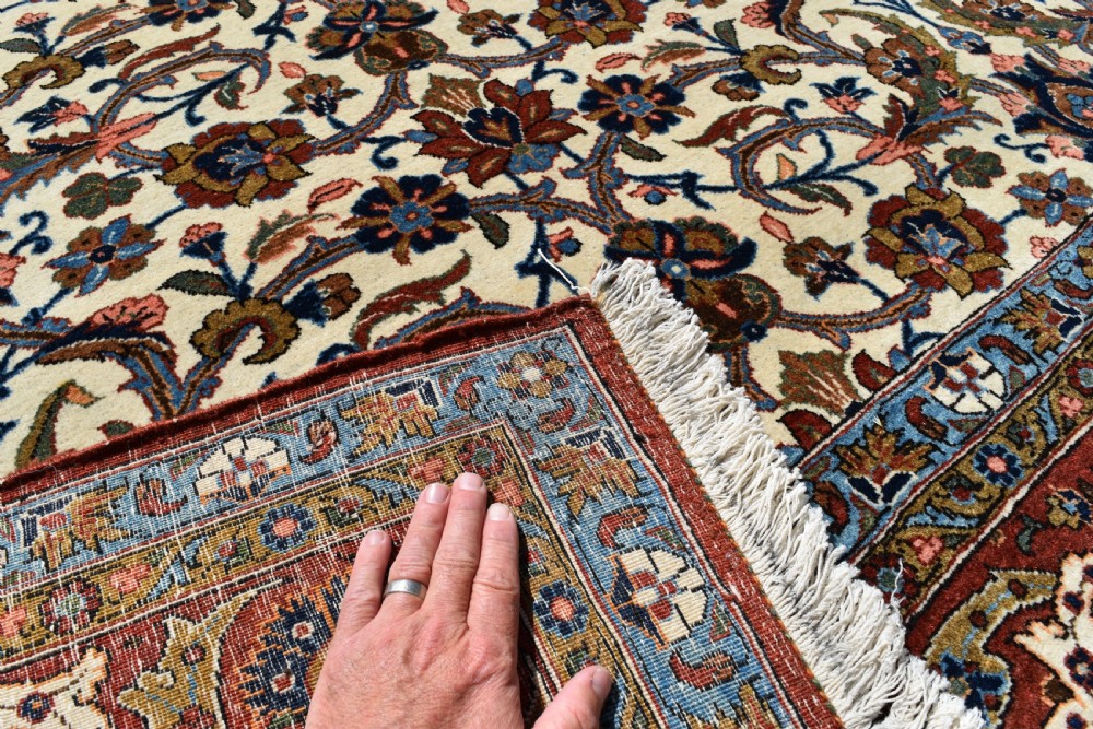A large hand-knotted Persian Qum carpet featuring an all-over intricate floral vine motif on an ivory field, framed by multi-tiered red and blue decorative borders with fringe ends. View VIII