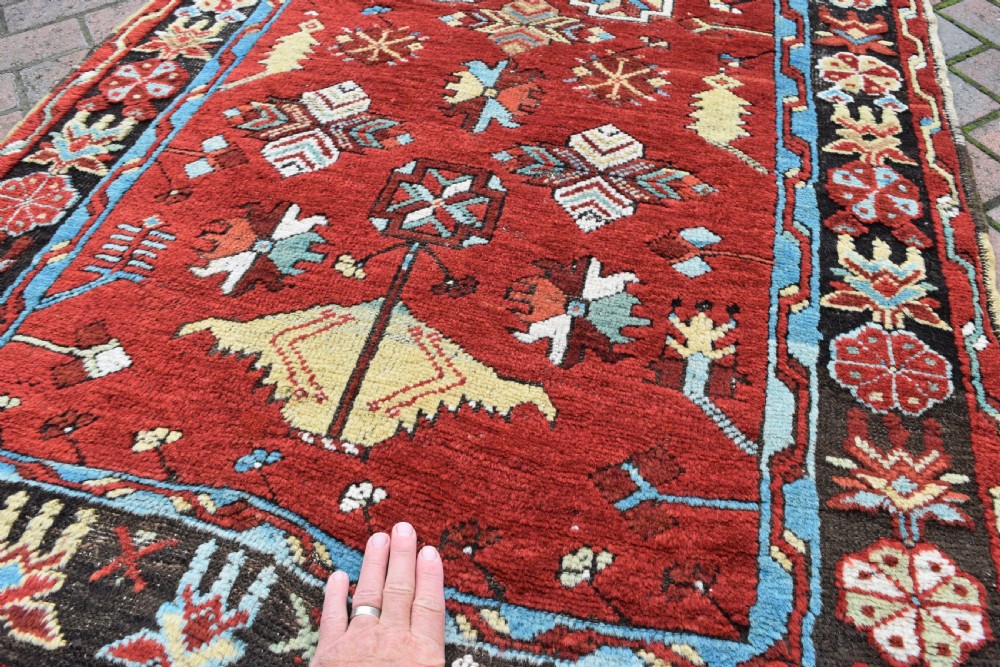 An antique long wool runner rug featuring a rich red field with geometric tribal motifs framed by a blue inner border and dark outer border. View II