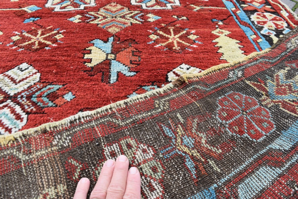 An antique long wool runner rug featuring a rich red field with geometric tribal motifs framed by a blue inner border and dark outer border. View IV
