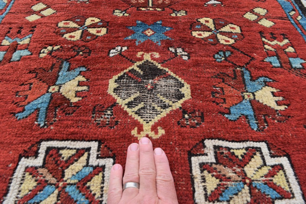 An antique long wool runner rug featuring a rich red field with geometric tribal motifs framed by a blue inner border and dark outer border. View V