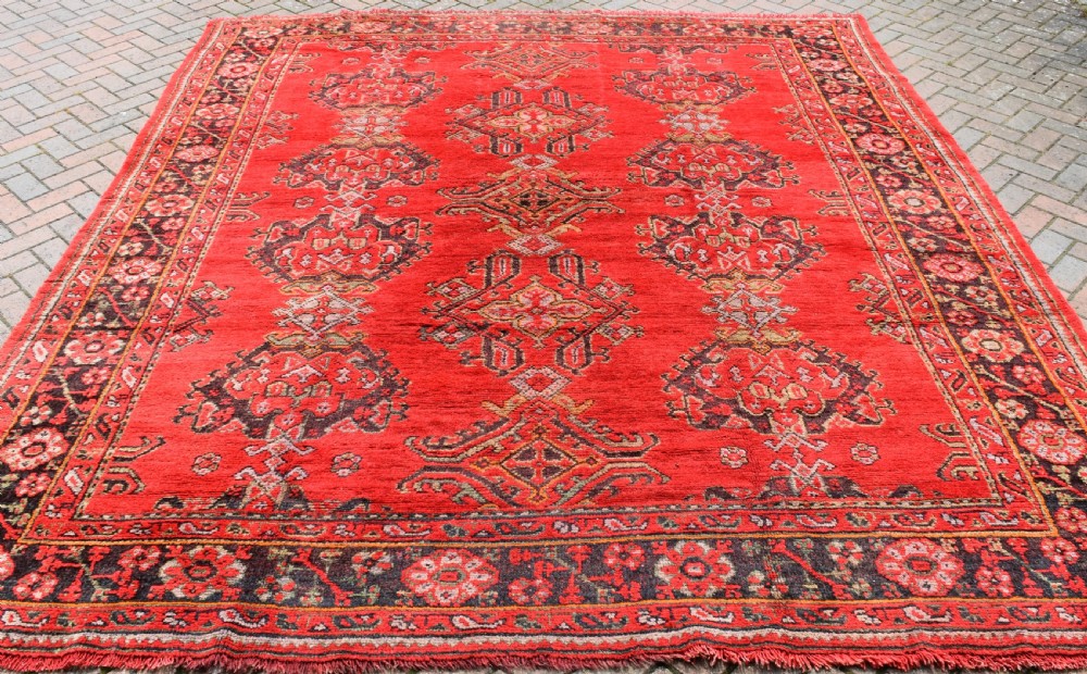 An antique hand-knotted Turkish Ushak wool carpet featuring a red field adorned with central geometric medallions and a patterned border.