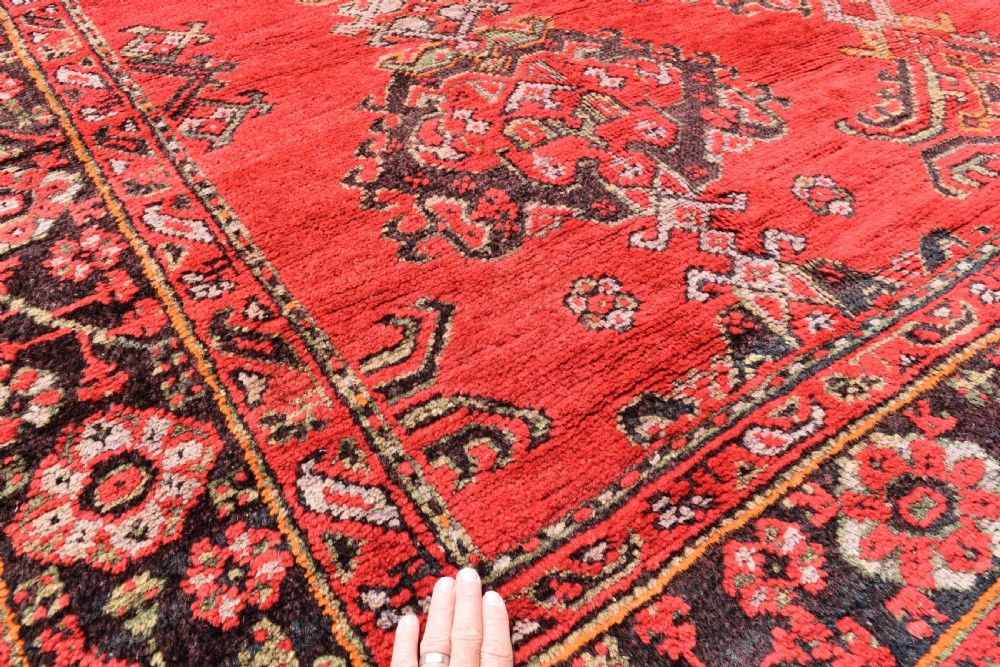 An antique hand-knotted Turkish Ushak wool carpet featuring a red field adorned with central geometric medallions and a patterned border. View II