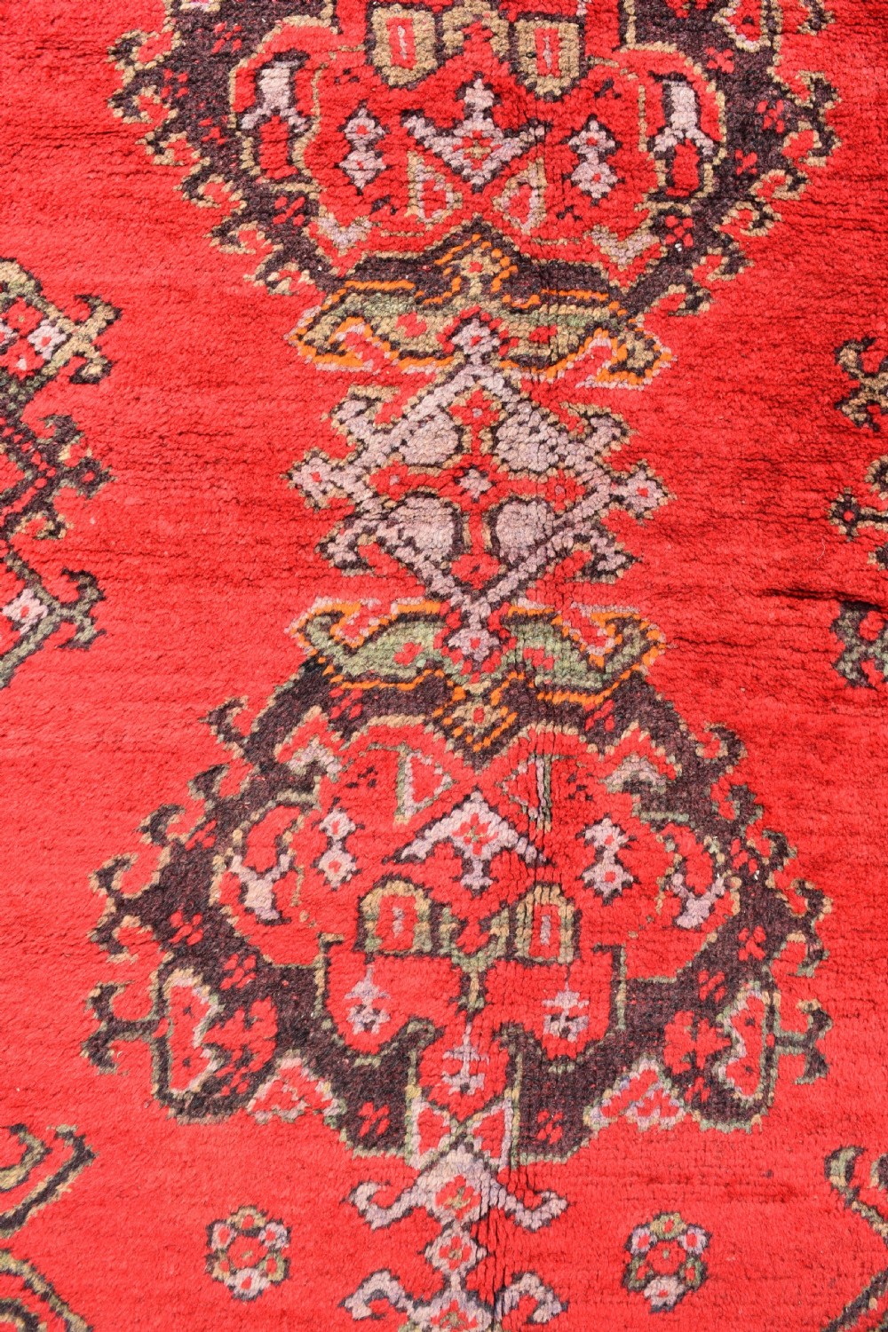 An antique hand-knotted Turkish Ushak wool carpet featuring a red field adorned with central geometric medallions and a patterned border. View III