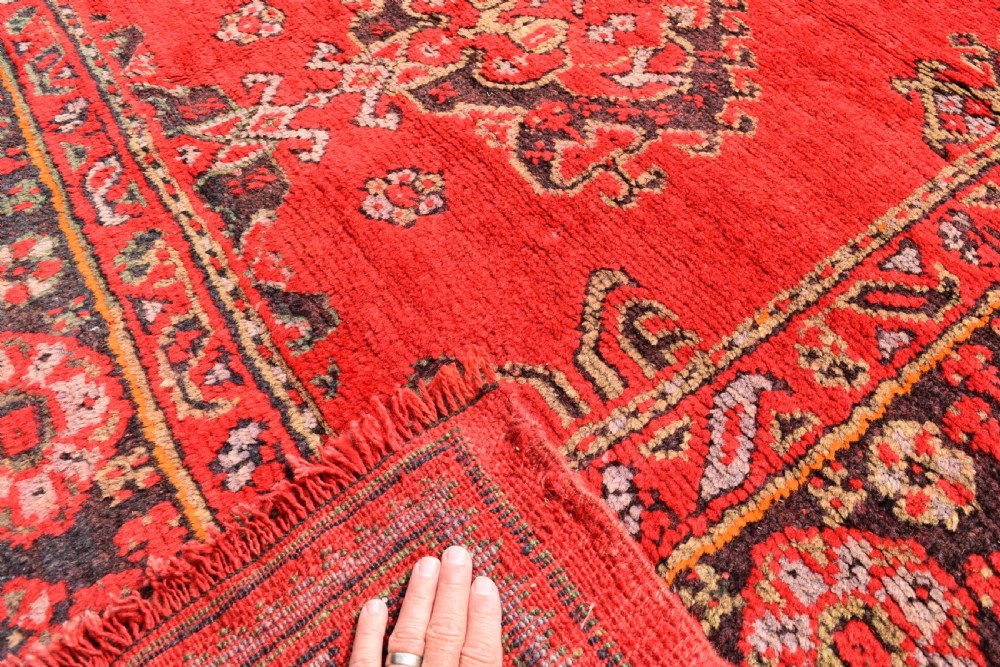 An antique hand-knotted Turkish Ushak wool carpet featuring a red field adorned with central geometric medallions and a patterned border. View V
