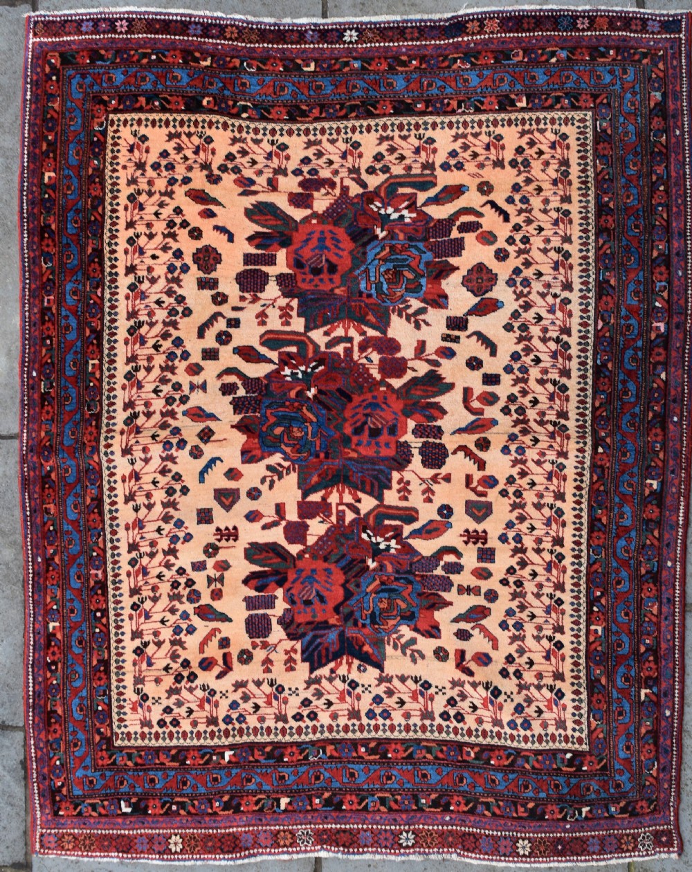 An antique hand-knotted Afshar rug featuring three central stylized floral medallions on a light peach field with intricate geometric borders in indigo and red.