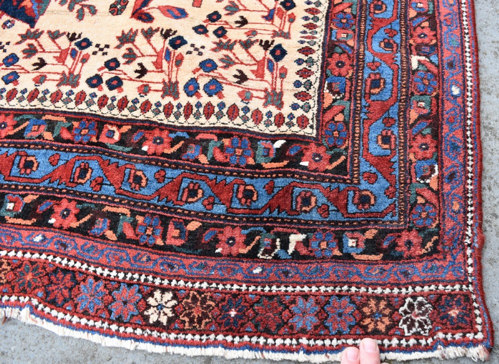 An antique hand-knotted Afshar rug featuring three central stylized floral medallions on a light peach field with intricate geometric borders in indigo and red. View IV