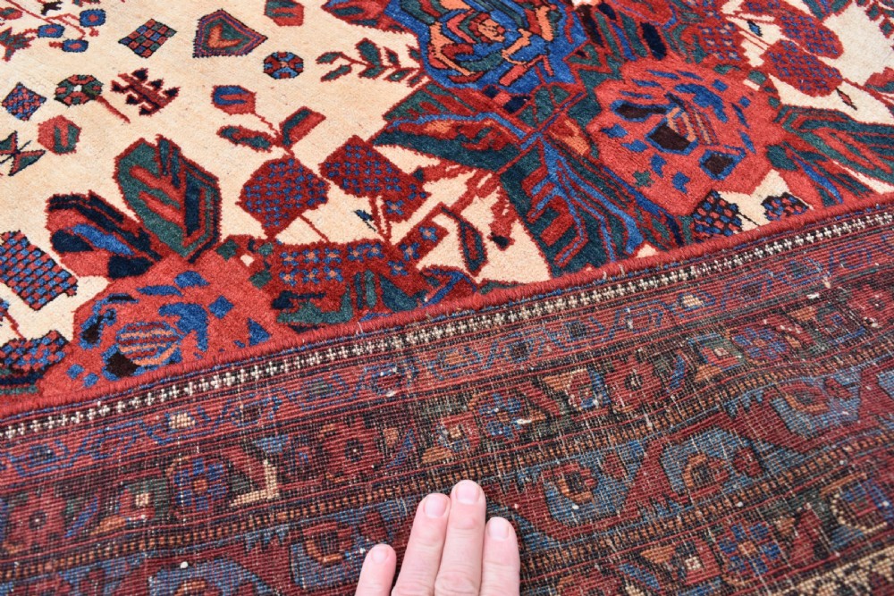 An antique hand-knotted Afshar rug featuring three central stylized floral medallions on a light peach field with intricate geometric borders in indigo and red. View VI