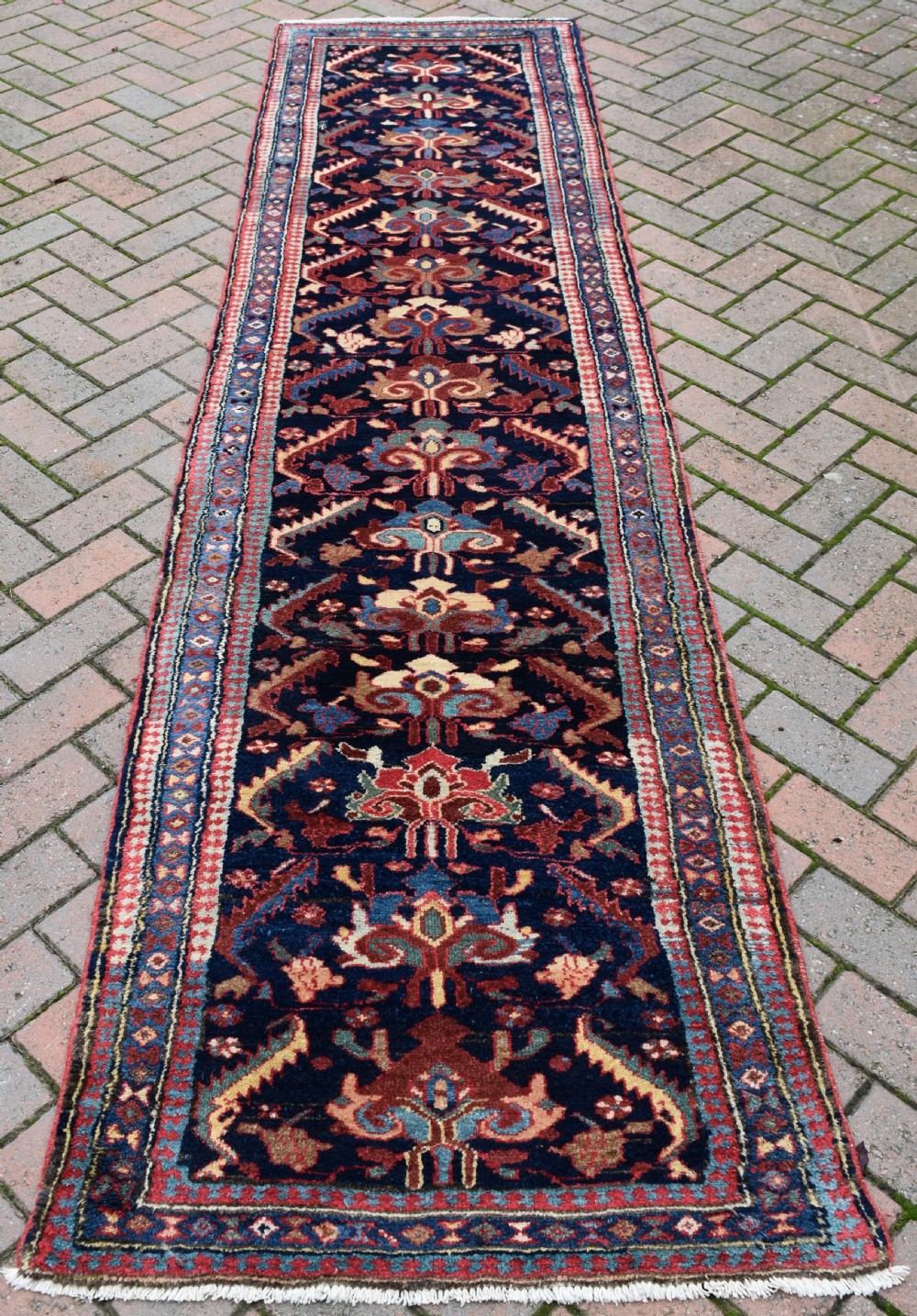 A long, narrow antique hand-knotted wool runner featuring intricate geometric floral motifs on a dark navy field bordered in terracotta and light blue.