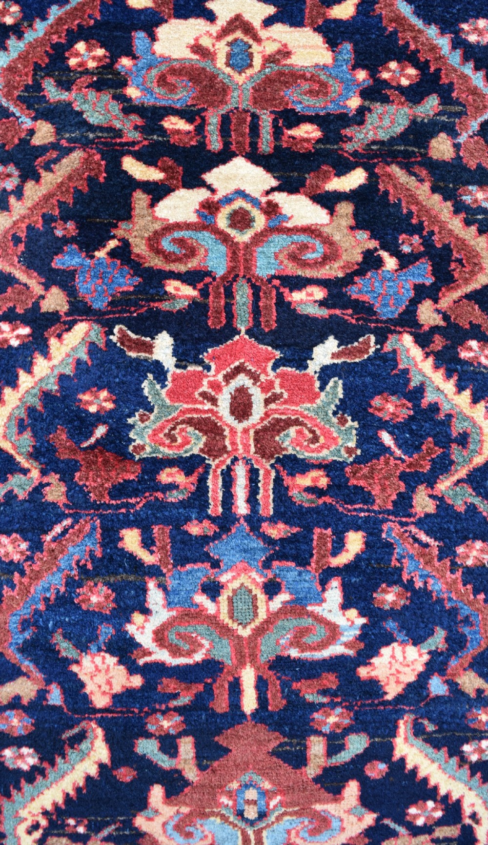 A long, narrow antique hand-knotted wool runner featuring intricate geometric floral motifs on a dark navy field bordered in terracotta and light blue. View II