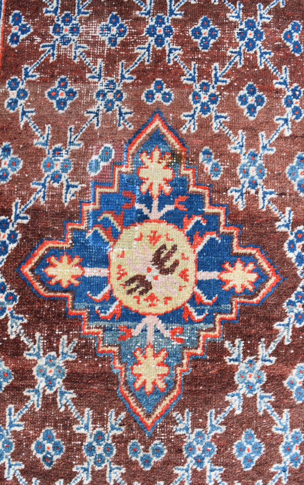 An extra long antique hand-knotted wool runner rug featuring a terracotta field patterned with repeating geometric florets and a central star emblem inside patterned borders. View III
