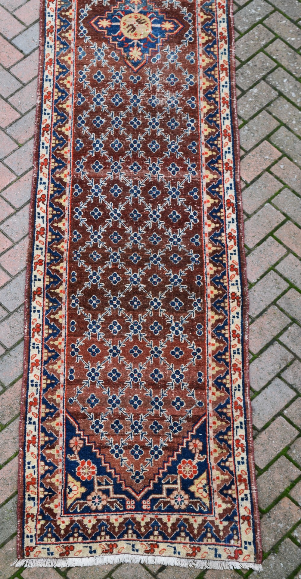 An extra long antique hand-knotted wool runner rug featuring a terracotta field patterned with repeating geometric florets and a central star emblem inside patterned borders. View V