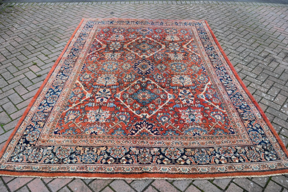 A hand-knotted Persian Mahal carpet featuring a terracotta central field with intricate floral and diamond medallions enclosed within a dark navy blue floral border.