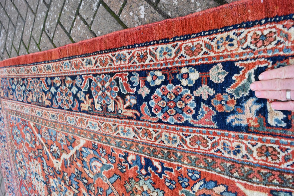 A hand-knotted Persian Mahal carpet featuring a terracotta central field with intricate floral and diamond medallions enclosed within a dark navy blue floral border. View IV