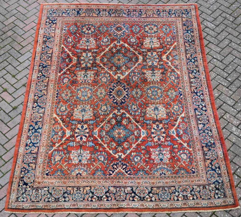 A hand-knotted Persian Mahal carpet featuring a terracotta central field with intricate floral and diamond medallions enclosed within a dark navy blue floral border. View V