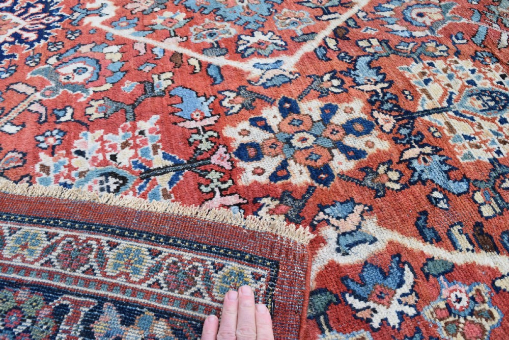 A hand-knotted Persian Mahal carpet featuring a terracotta central field with intricate floral and diamond medallions enclosed within a dark navy blue floral border. View VI