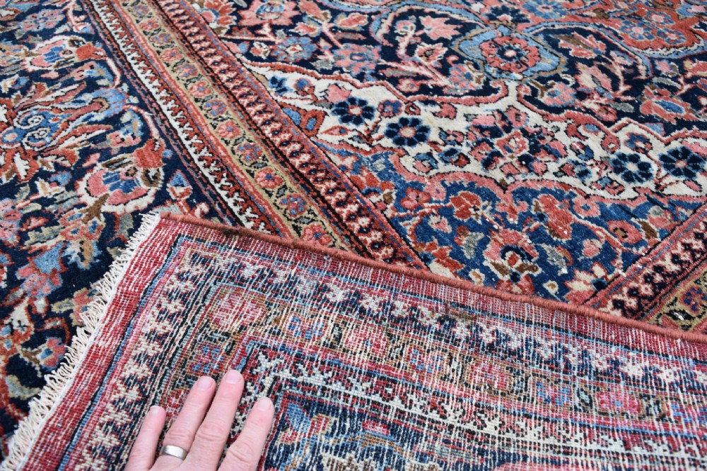 A large hand-knotted antique Kashan wool carpet featuring a central cream and blue medallion surrounded by dense floral patterns on a terracotta red field with decorative multi-tiered borders. View II