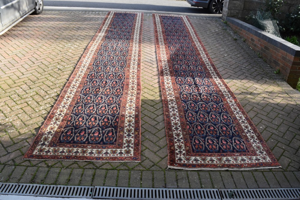 A matching pair of long antique Malayer hand-knotted wool runner rugs displaying repeating geometric boteh motifs in navy blue, terracotta red, and ivory. View II