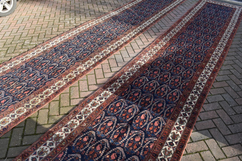 A matching pair of long antique Malayer hand-knotted wool runner rugs displaying repeating geometric boteh motifs in navy blue, terracotta red, and ivory. View IV