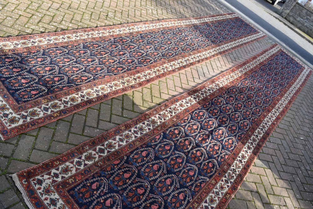 A matching pair of long antique Malayer hand-knotted wool runner rugs displaying repeating geometric boteh motifs in navy blue, terracotta red, and ivory. View V
