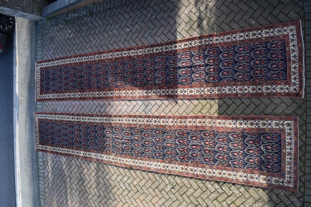 A matching pair of long antique Malayer hand-knotted wool runner rugs displaying repeating geometric boteh motifs in navy blue, terracotta red, and ivory. View VI