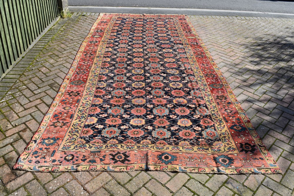An elongated hand-knotted antique wool Kurdish Kelleh carpet featuring a repeating floral lattice pattern on a dark navy field surrounded by a patterned red border.