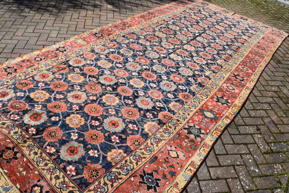 An elongated hand-knotted antique wool Kurdish Kelleh carpet featuring a repeating floral lattice pattern on a dark navy field surrounded by a patterned red border. View IV