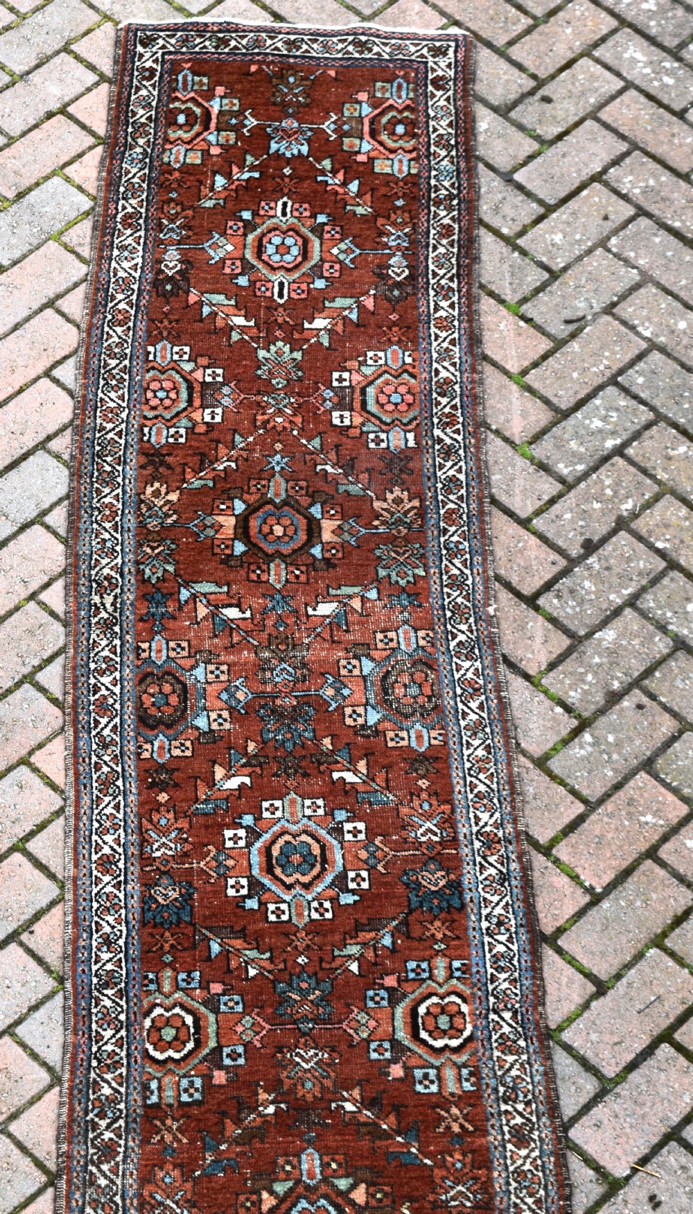 An antique hand-knotted Persian Gorravan wool runner rug featuring repeating geometric medallions in blue, pink, and turquoise across a rust-red field with geometric border bands. View II