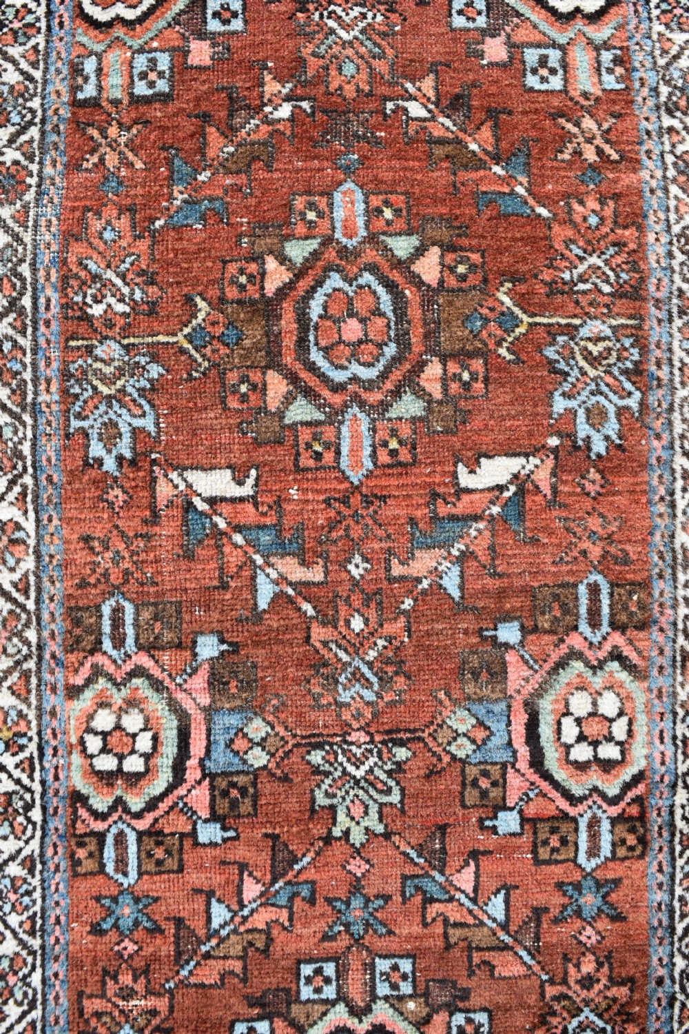 An antique hand-knotted Persian Gorravan wool runner rug featuring repeating geometric medallions in blue, pink, and turquoise across a rust-red field with geometric border bands. View IV