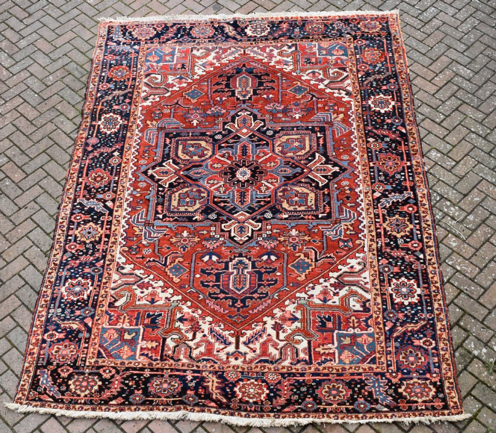 An antique Persian Heriz hand-knotted wool rug featuring a large geometric central medallion in navy blue, rust red, and cream tones.