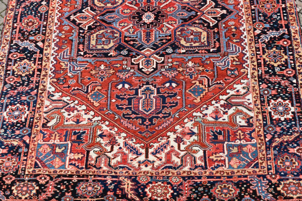 An antique Persian Heriz hand-knotted wool rug featuring a large geometric central medallion in navy blue, rust red, and cream tones. View II