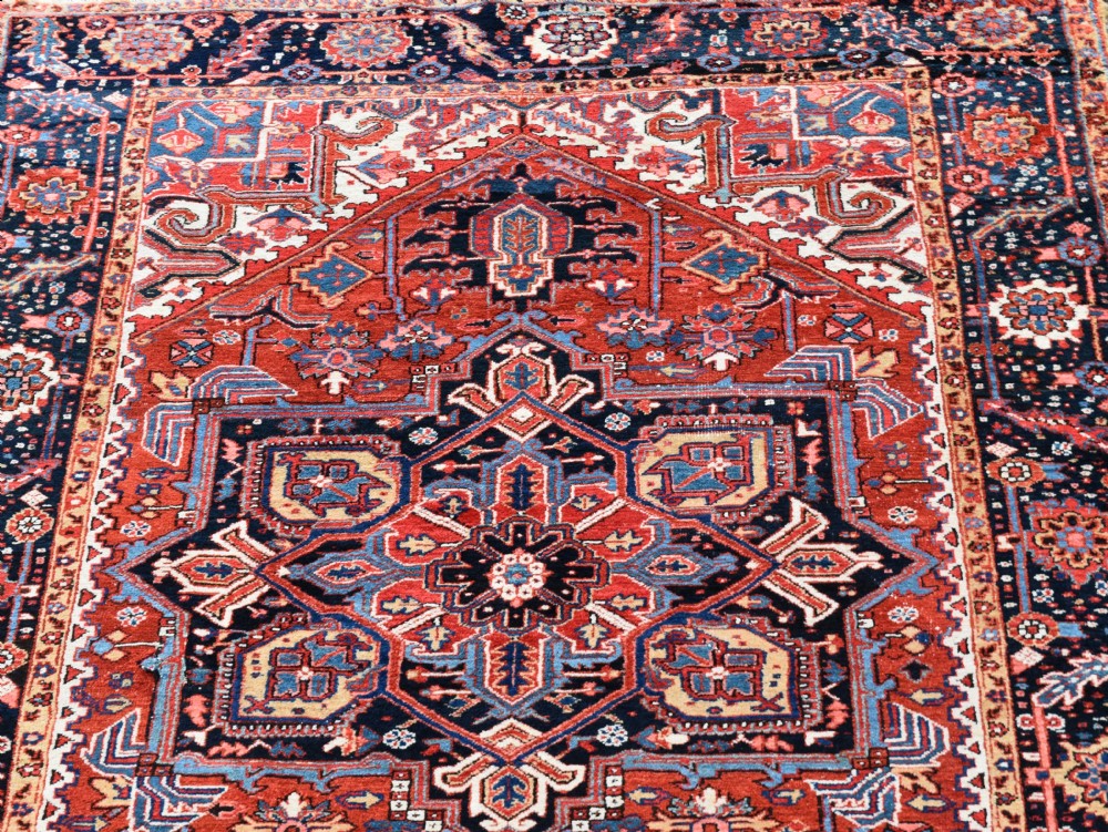 An antique Persian Heriz hand-knotted wool rug featuring a large geometric central medallion in navy blue, rust red, and cream tones. View III